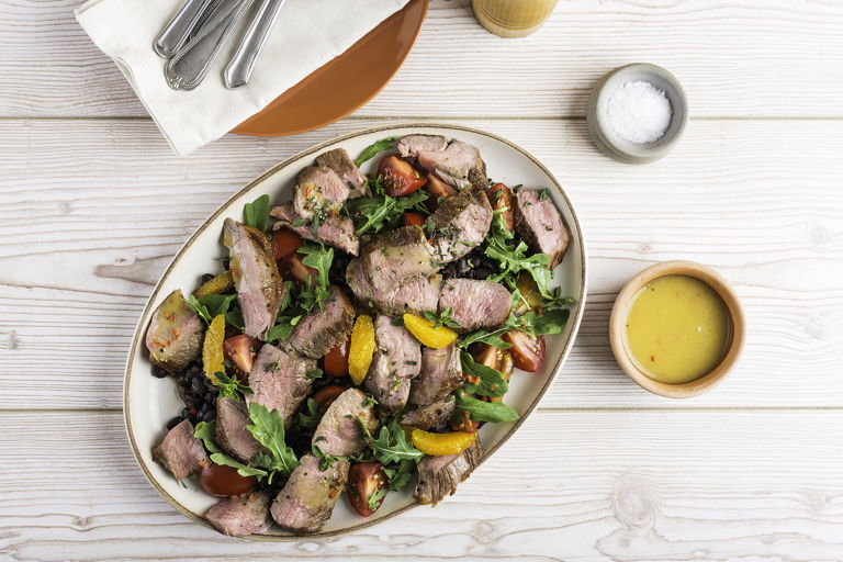 Warm salad of slice lamb leg steak, tomato and black beans with a chilli and orange dressing