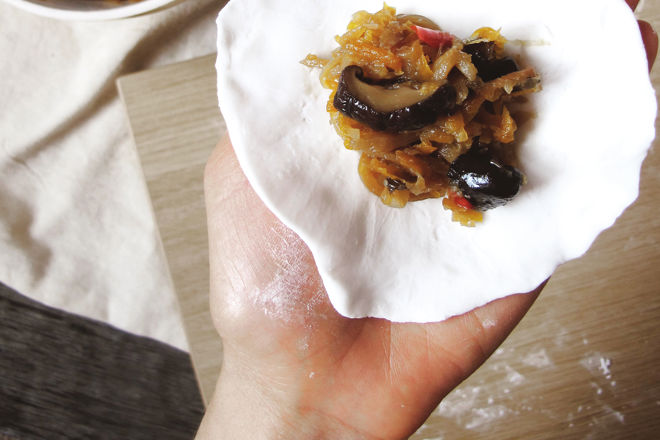 Hands shaping homemade Canederli dough with cubes of bread, speck, and parsley on a wooden board